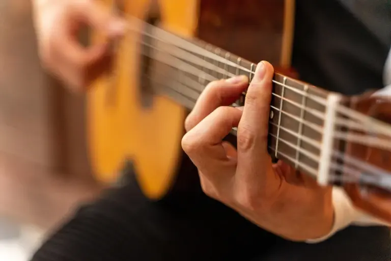 Close-up of a guitarist's hand pressing strings on the neck of an acoustic guitar, highlighting wood grain and string interaction.