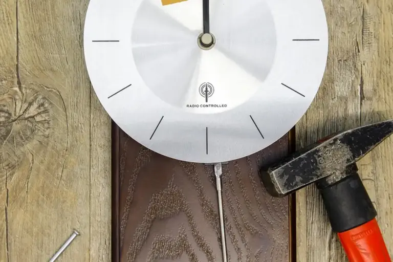 A round, silver dial gauge mounted on weathered wooden planks, with a hammer nearby, representing at-home testing of adhesive bond strength for wood projects.