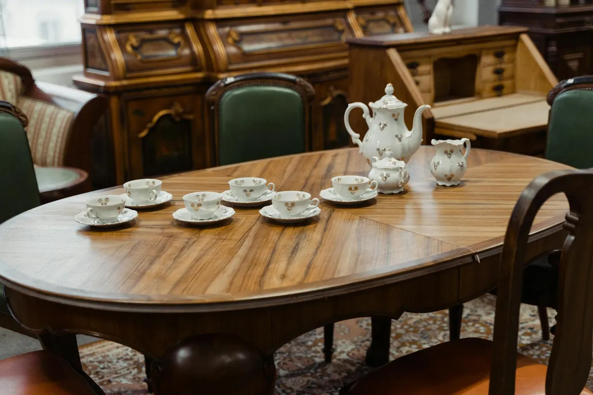 An oval wooden antique dining table with a white porcelain tea set in a traditional room.