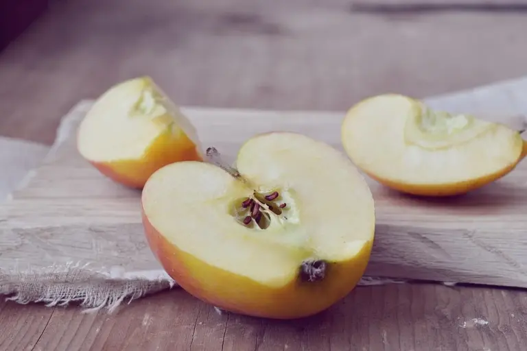 Two halved apples on a wooden cutting board with a textured surface.