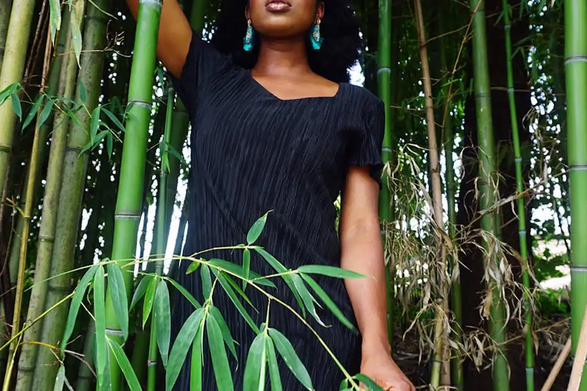 A person in a dark dress stands among tall green bamboo stalks in a lush grove.