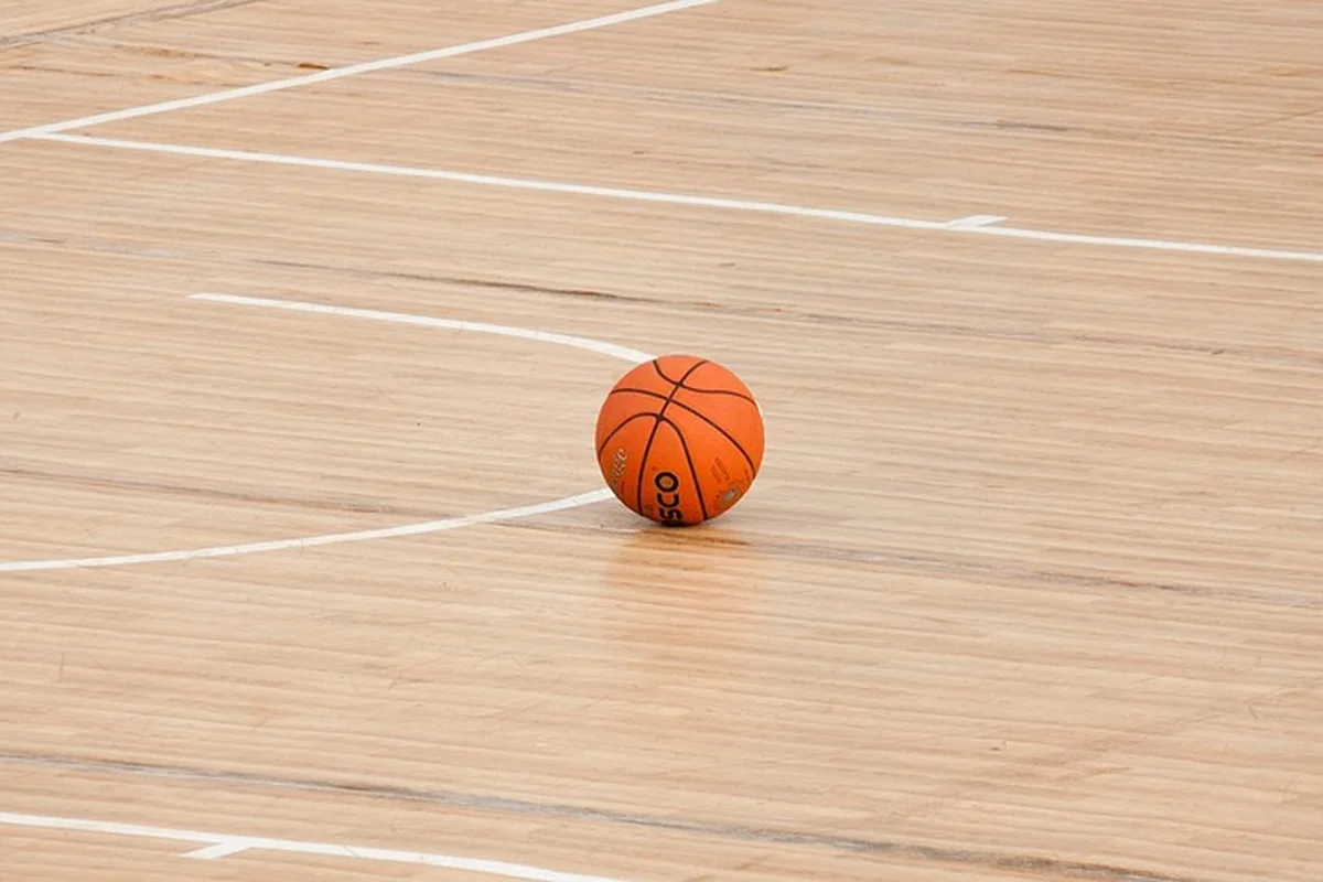 Basketball resting on a light hardwood gym floor with court lines