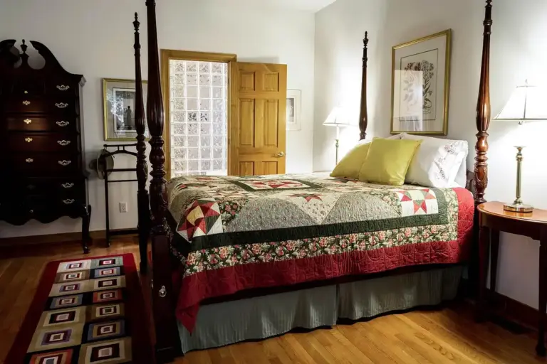 A traditional bedroom with a four-poster bed, patchwork quilt, and hardwood floors.