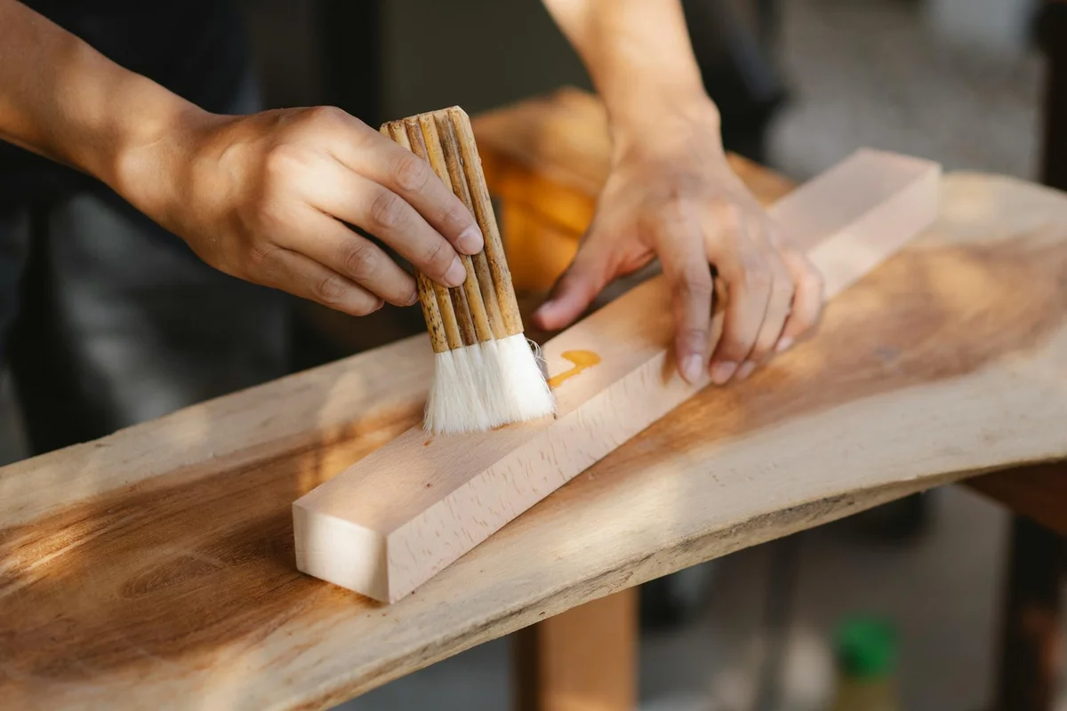 Hands applying oil to a wooden board with a brush in a workshop