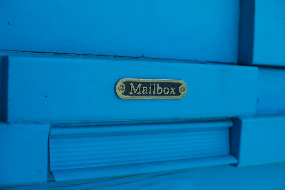 Close-up of a blue-painted wooden mailbox with a brass plaque labeled 'Mailbox'.