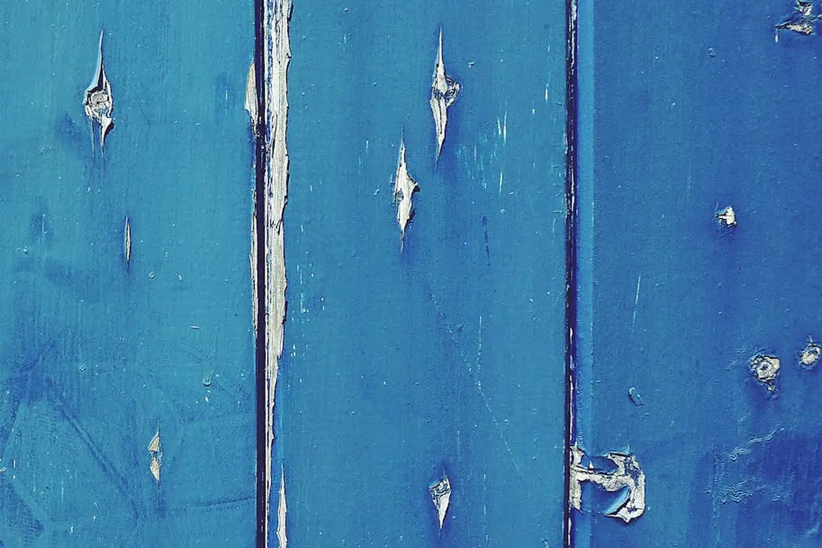 Close-up of weathered blue-painted wooden boards with chipped and peeling paint and visible grain.