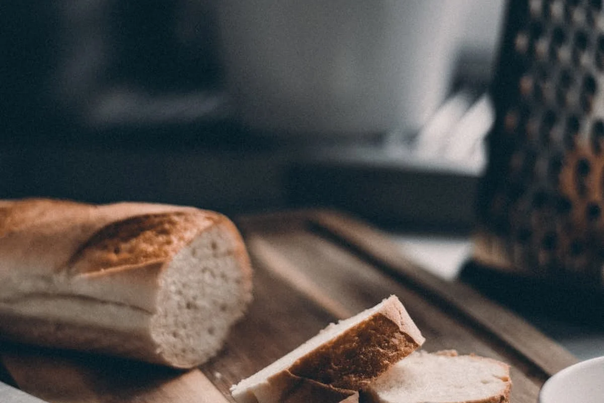 Sliced bread on a wooden cutting board with a blurred metal grater in the background.