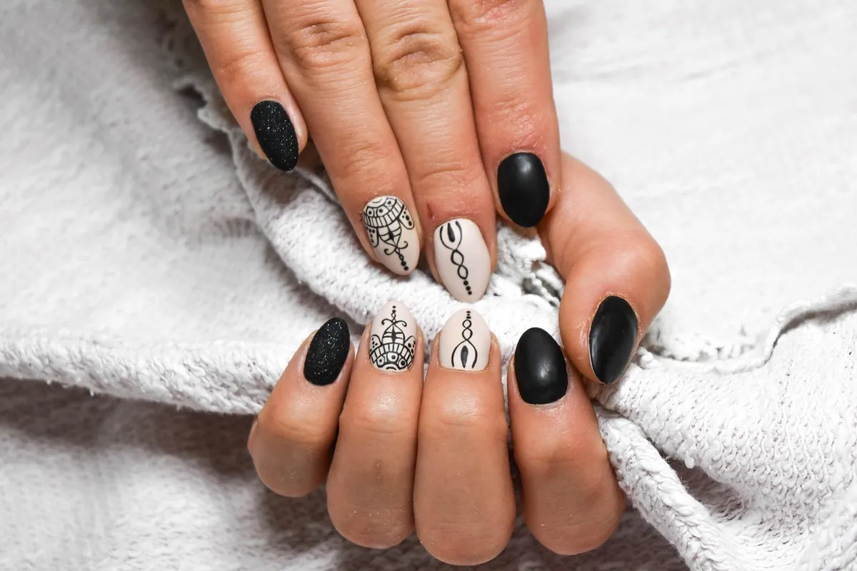 Close-up of hands with a two-tone manicure: black matte nails and white accent nails with delicate line-art designs on a soft gray towel.