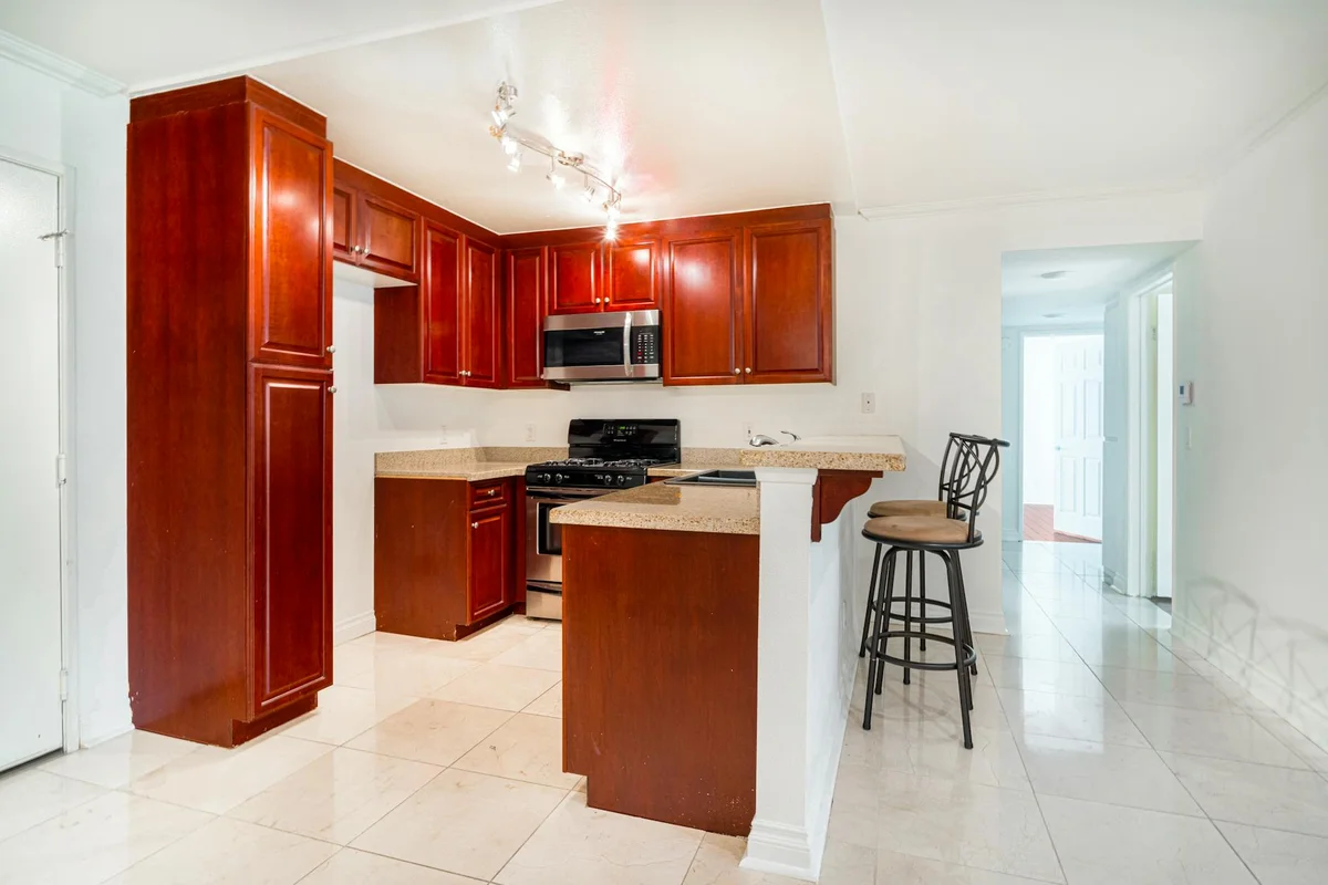 Kitchen with rich cherry wood cabinets, light countertops, and white tile flooring.