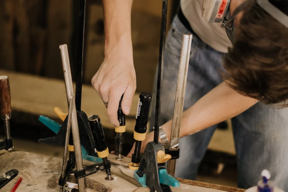 Close-up of hands tightening clamps on a wood glue-up, with multiple clamps applying even pressure to bound pieces