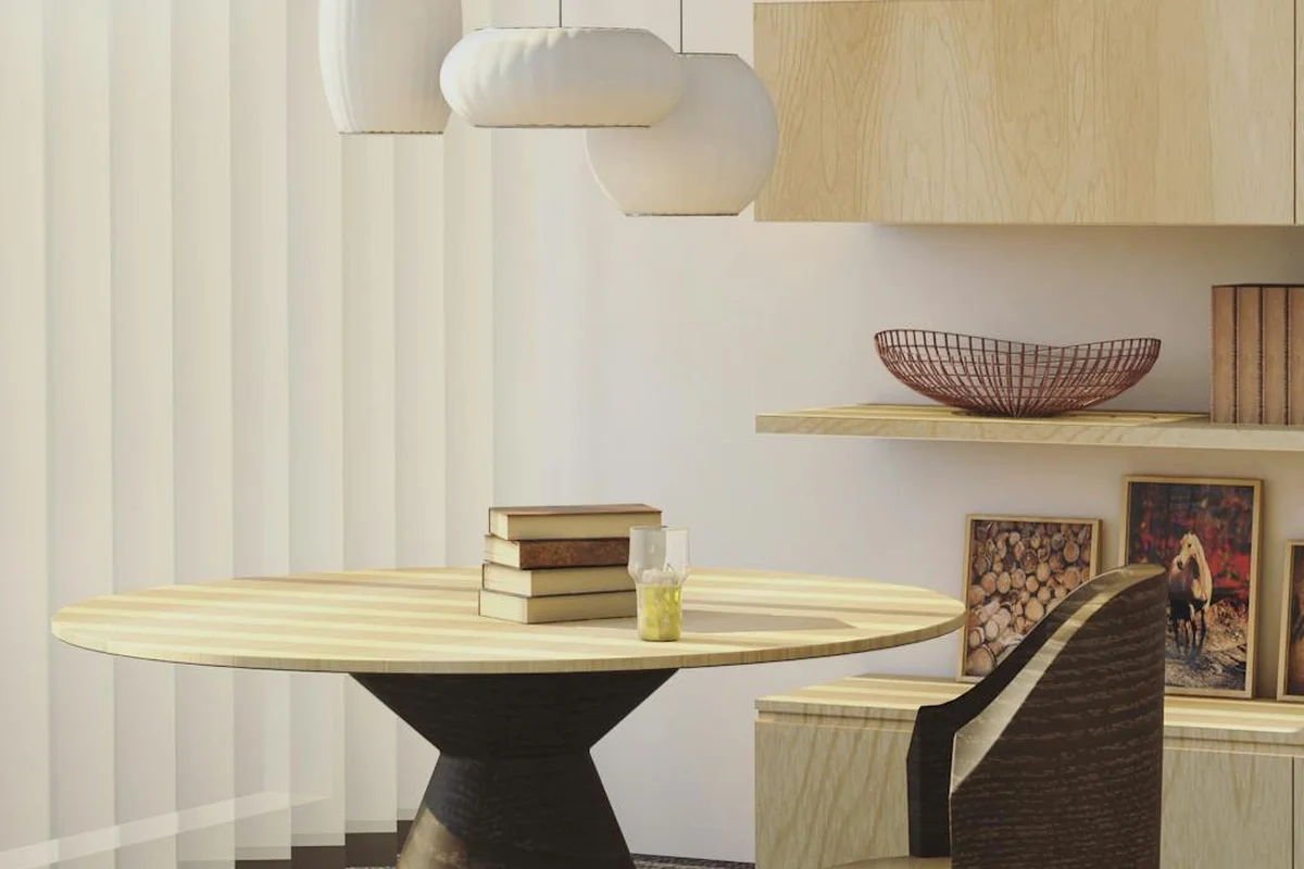 Modern dining area with a round light-wood table and matching chair in a coastal-inspired, neutral-toned room.