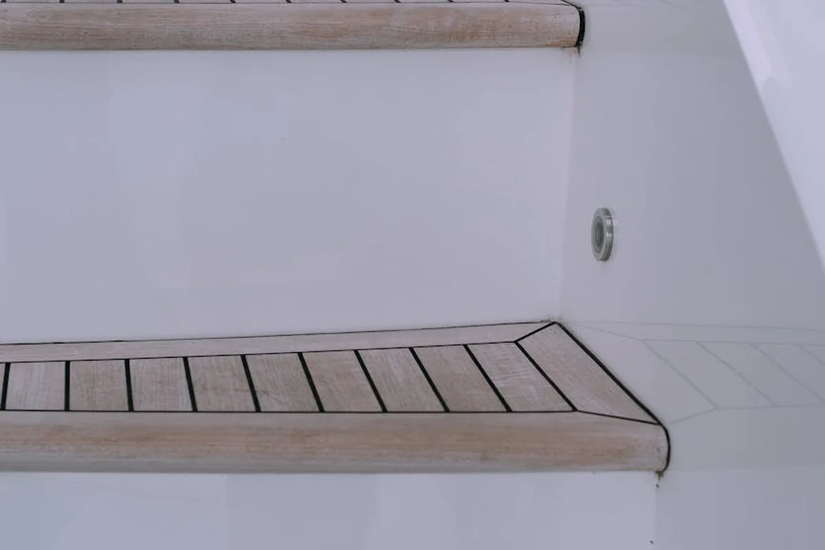 Light brown teak boat deck stairs with dark non-slip strips on a white boat hull.