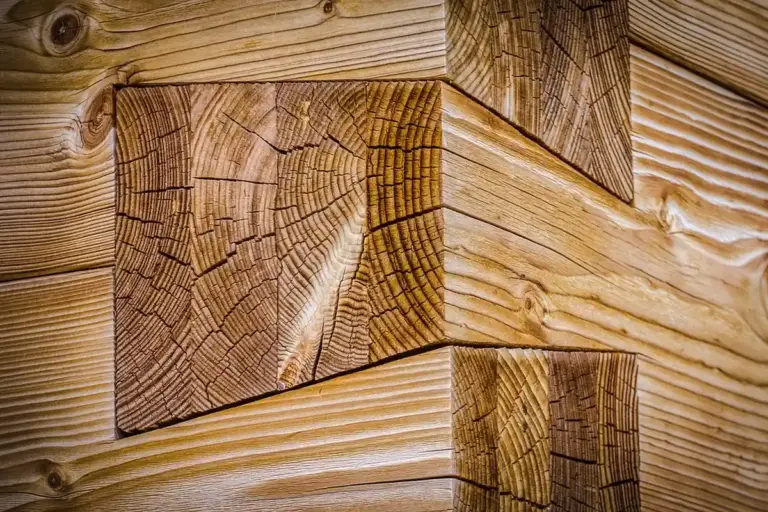 Close-up of a wooden corner joint showing visible growth rings, end grain, and beveled edges in a stacked log-frame style.