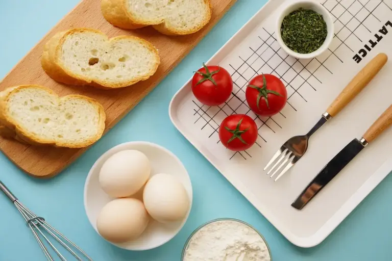 Bread slices on a wooden cutting board with eggs and tomatoes on a bright blue countertop.
