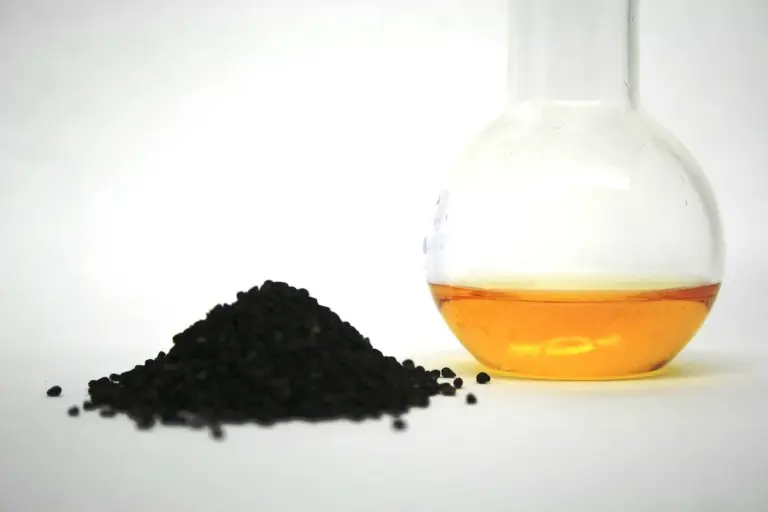 Beaker containing amber Danish oil beside a small pile of black granules on a white surface.