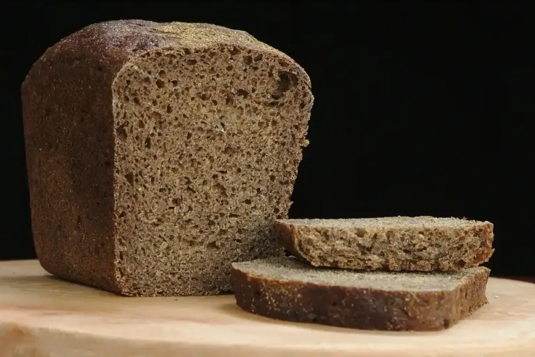Dark loaf of bread on a wooden cutting board with slices nearby, illustrating everyday use of a cutting board