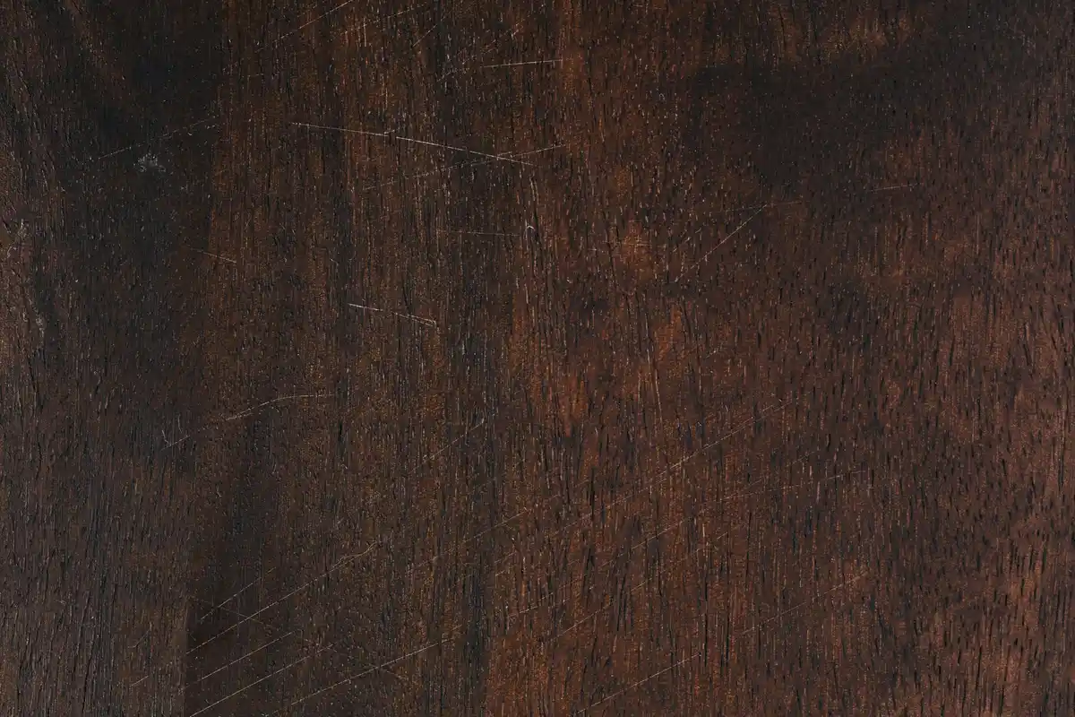 Close-up of a dark brown wood surface with visible grain and scratches.