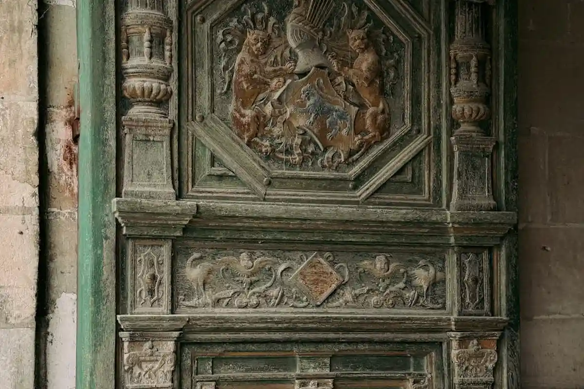 Ornate, weathered carved wooden door with a green patina and detailed relief panels.