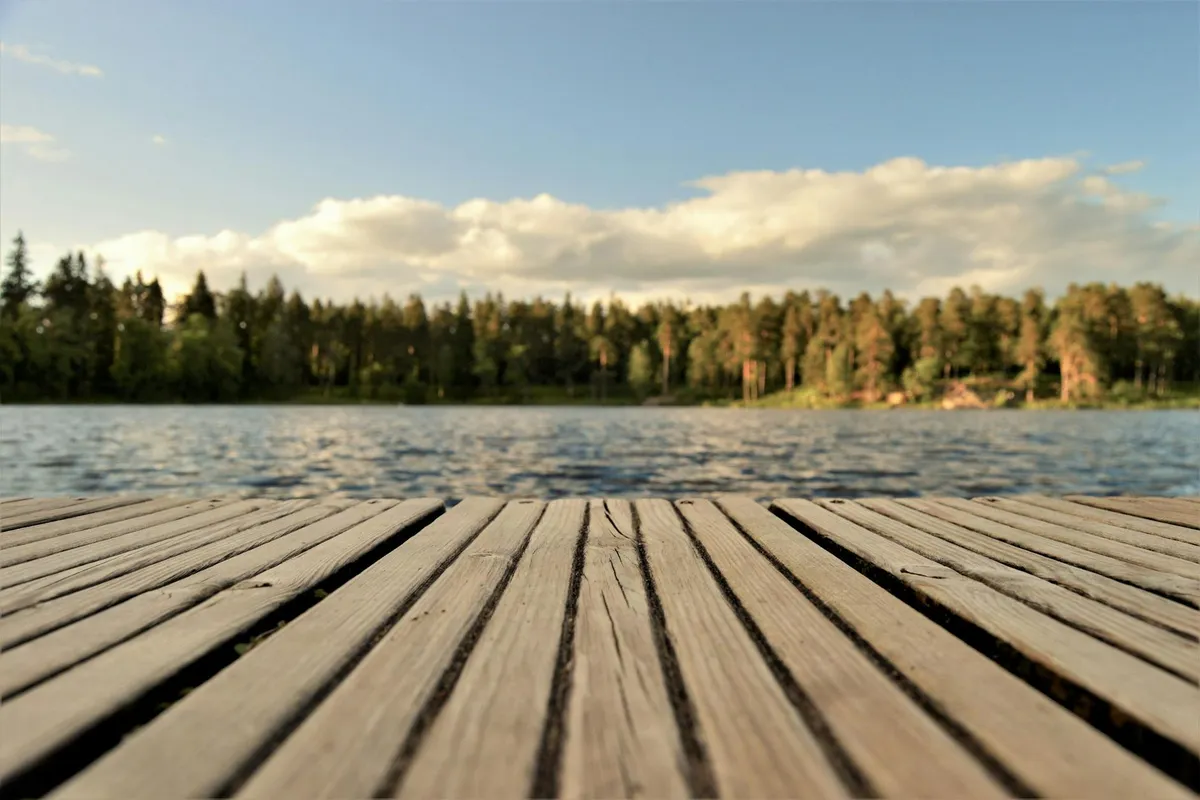 Close-up view of weather-resistant wooden dock planks extending toward a calm lake with a forested shoreline in the background.