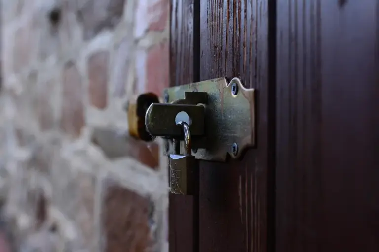 Close-up of a wooden door with a metal latch and strike plate mounted on a stone wall, illustrating common hardware affected by rot and warping.