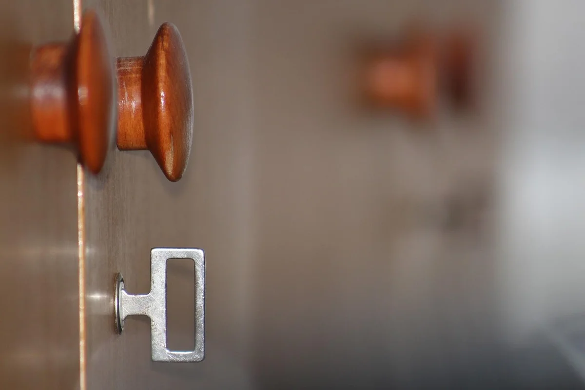 Close-up of a wooden door knob and a metal latch on a door with a blurred background