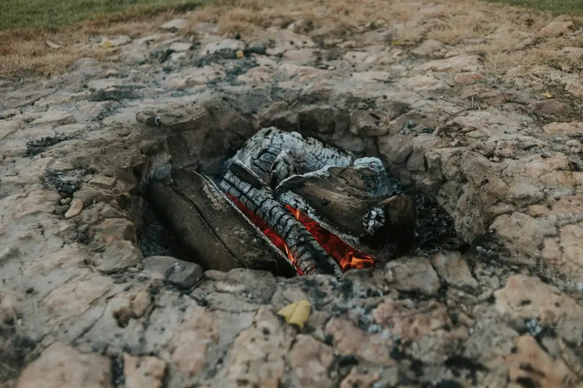 Circular hole in cracked earth with glowing embers and charred fragments