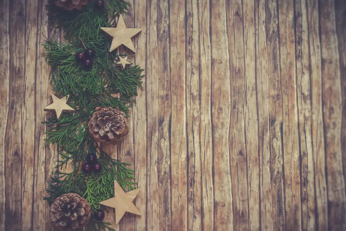 Festive evergreen garland with pinecones and wooden stars on a weathered wooden plank background.