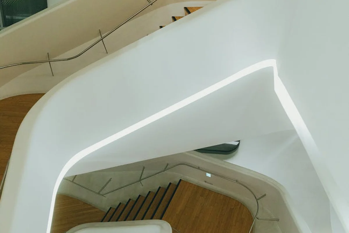 A modern interior detail showing a white curved surface beside cherry wood stair treads.