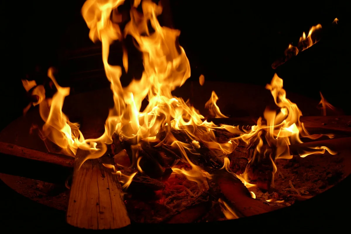 A wood fire burning in a fire pit at night with bright orange flames