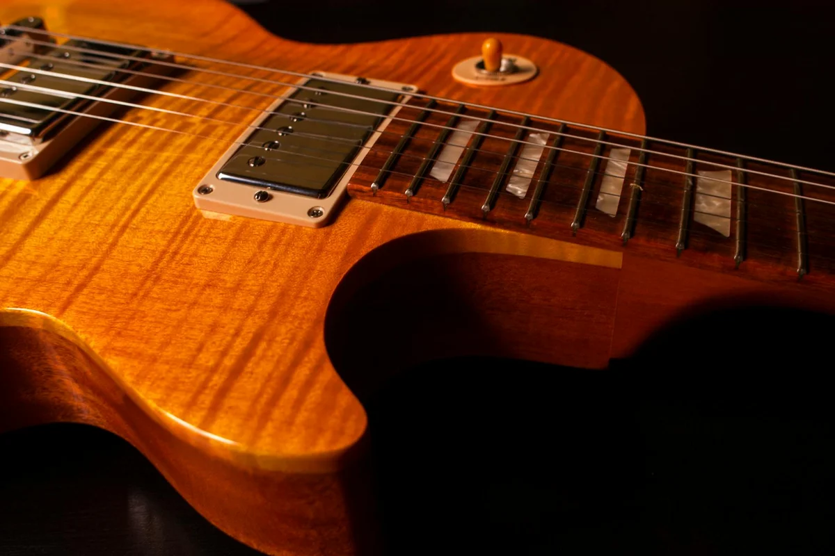 Close-up of a warm amber wooden guitar body with a glossy finish, showing the wood grain and reflections.