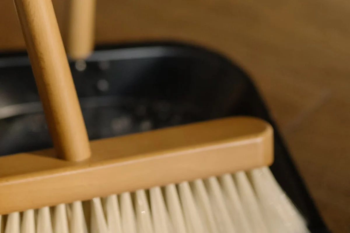 Close-up of a wooden-handled floor brush with light-colored bristles, resting in a dark basin or tray.