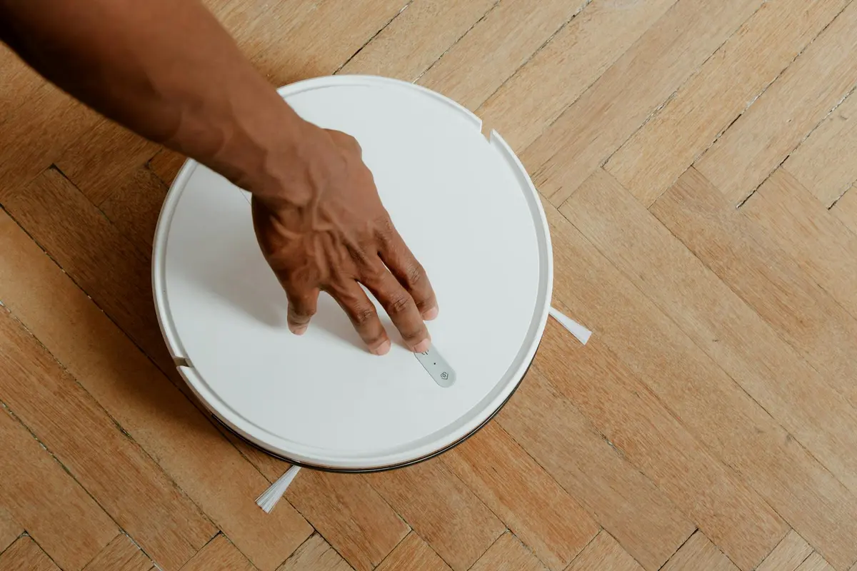 Hand pressing a round white disk on a wooden floor, illustrating a controlled, physics-based approach to locating and addressing squeaky floorboards.