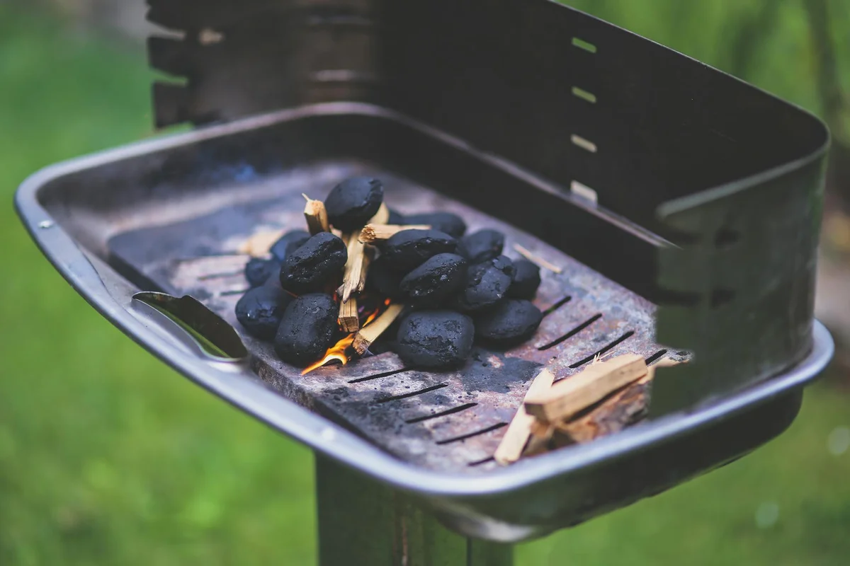 Barbecue grill basket filled with charcoal and wood chips, outdoors on a green lawn.