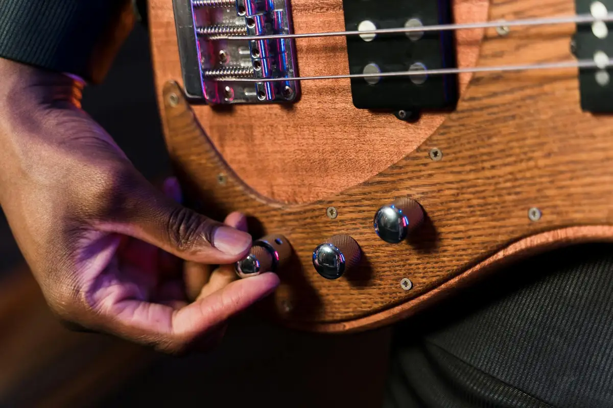 Close-up of a hand turning a control knob on a wooden guitar body, highlighting the wood grain and finish.