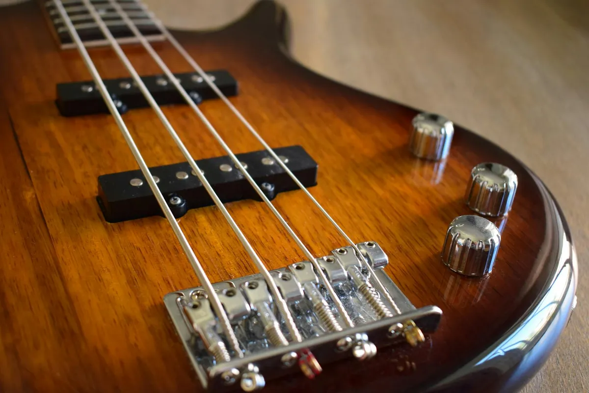 Close-up of a honey-colored wooden guitar with strings, pickups, and chrome bridge, showing wood grain and finish.