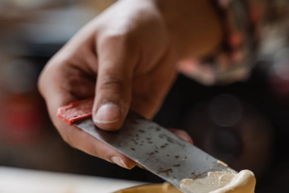 Close-up of a hand holding a putty knife applying wood filler