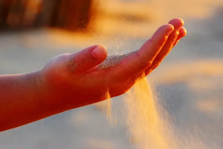 Close-up of a hand releasing fine sanding dust, illustrating the sanding process used to prepare wood for staining.