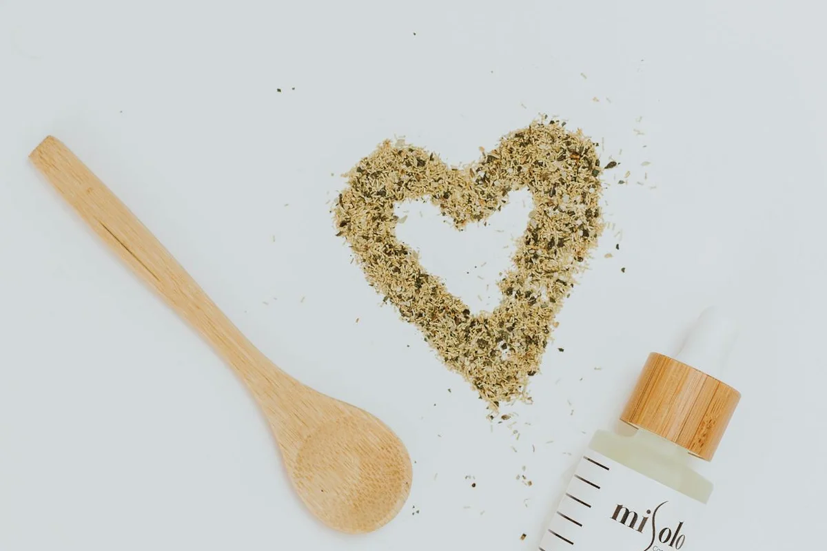 A wooden spoon, a bottle of oil with dropper, and a heart-shaped mound of fine powder on a light background, illustrating a practical oil finish comparison in woodworking.