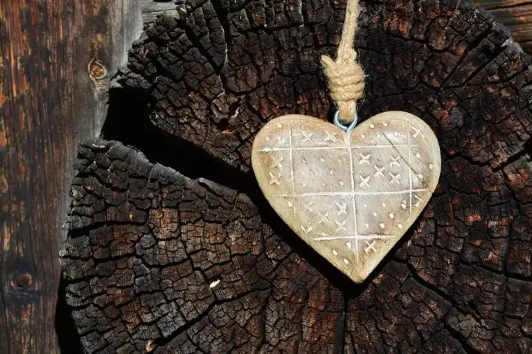 Heart-shaped pendant with carved patterns hangs from a rope against a weathered tree stump cross-section.