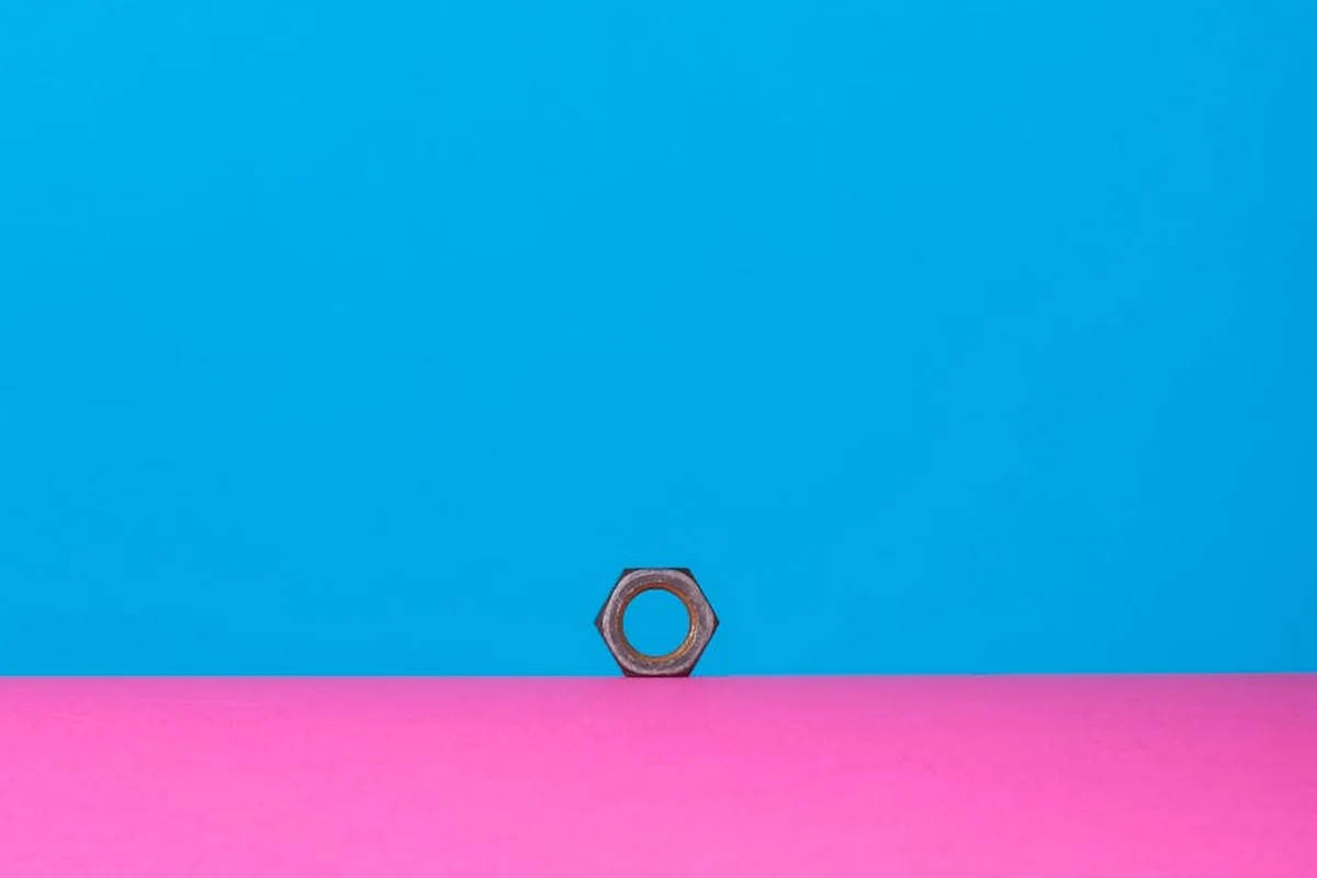 Close-up of a single hex nut on a blue and pink color-blocked background, with the nut positioned near the boundary.