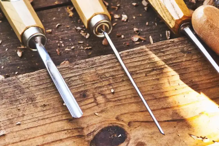Close-up of three wood chisels with wooden handles resting on a weathered wooden surface, representing the hands-on tools used in repairing historic woodwork with attention to structural integrity, material authenticity, and reversibility.