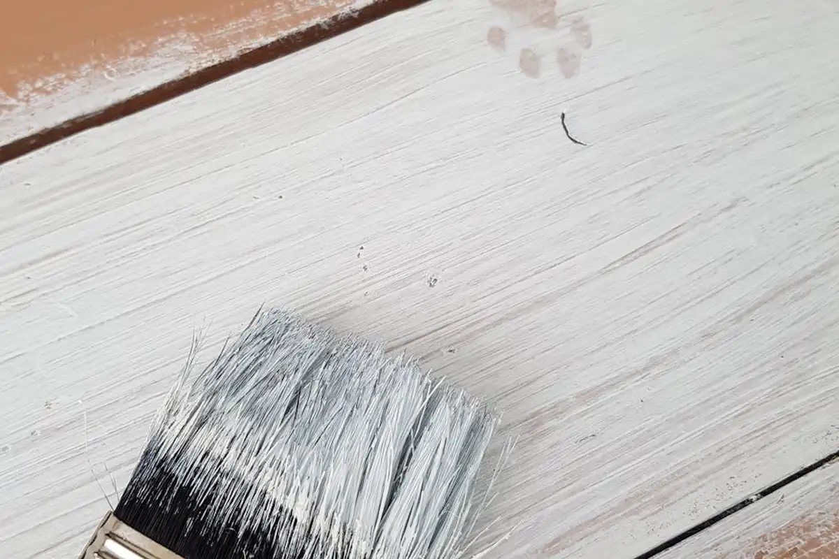 Close-up of a paintbrush resting on light gray wooden boards, illustrating reversible finishes needed in historic woodwork repair.