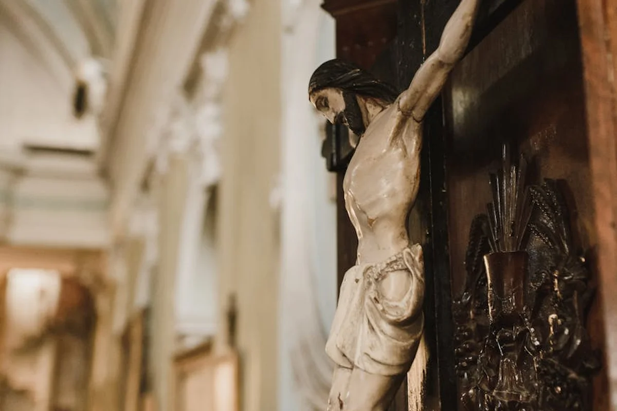 Close-up of a carved wooden crucifix mounted on a dark panel in a historic church interior with a blurred architectural background.