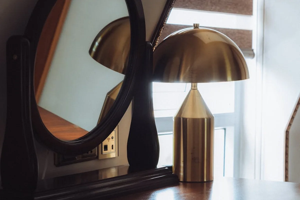 Brass desk lamp on a wooden surface with a mirror and window light.