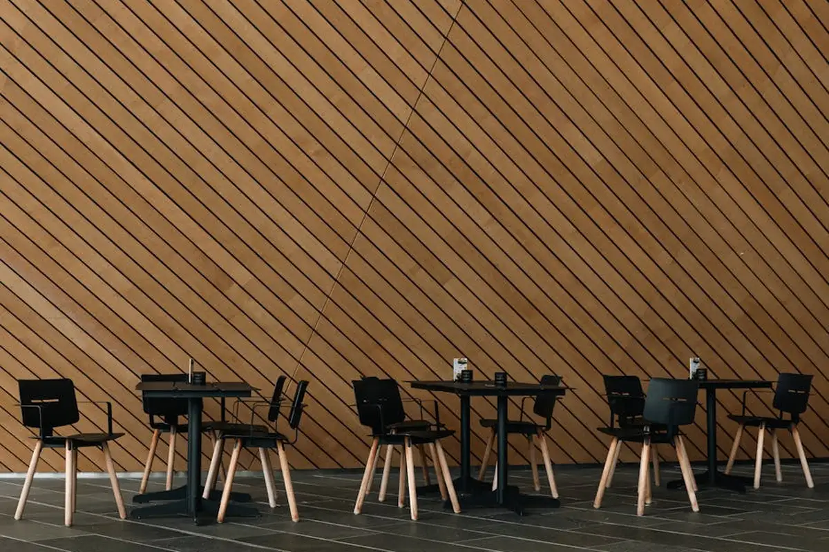 Interior space with a diagonally arranged wooden slat wall and minimalist black tables and chairs