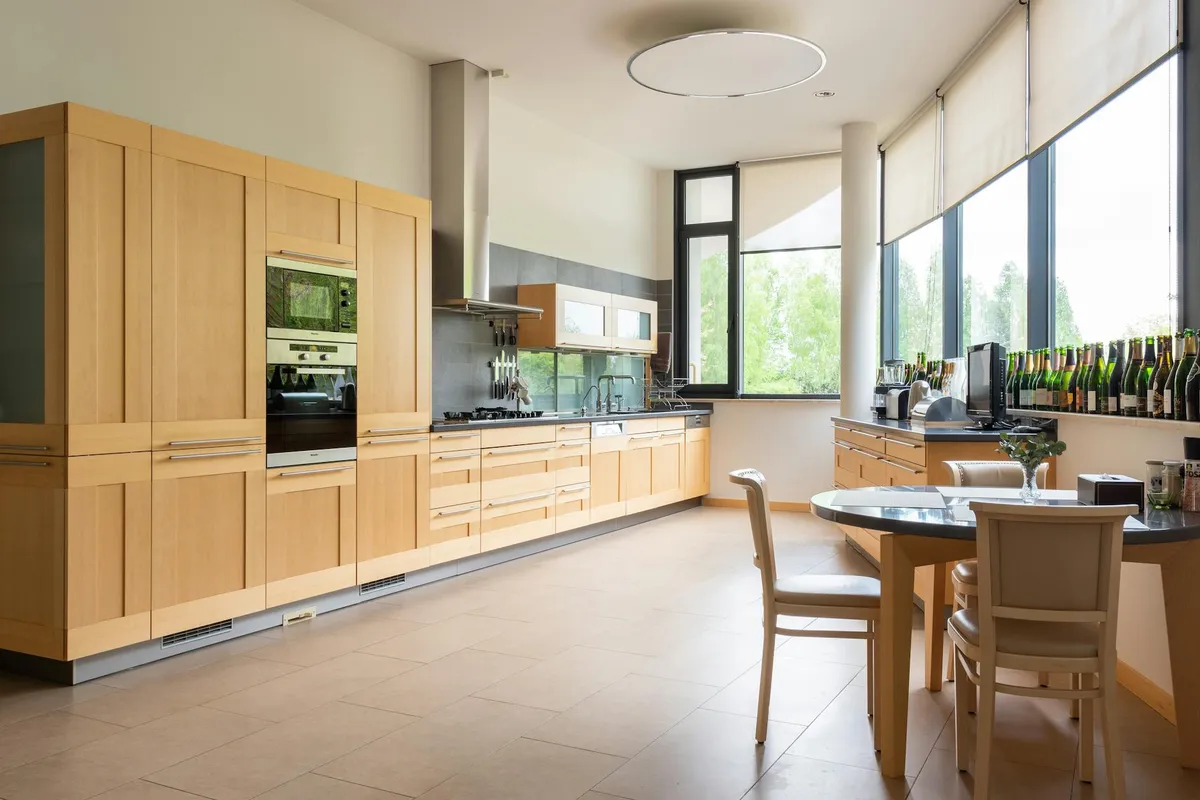 Bright, modern kitchen with light wood cabinetry, a round dining table, and large windows letting in natural light.