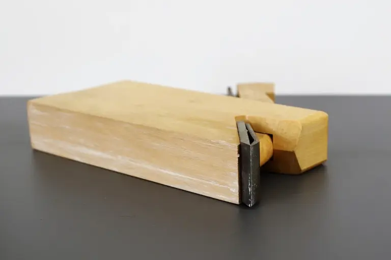 A wooden-handled scraper tool with a metal blade used to strip lacquer from wood furniture
