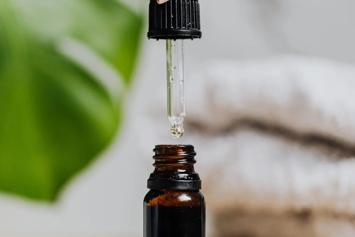 Close-up of a dropper releasing linseed oil into a dark amber bottle, with a blurred background.