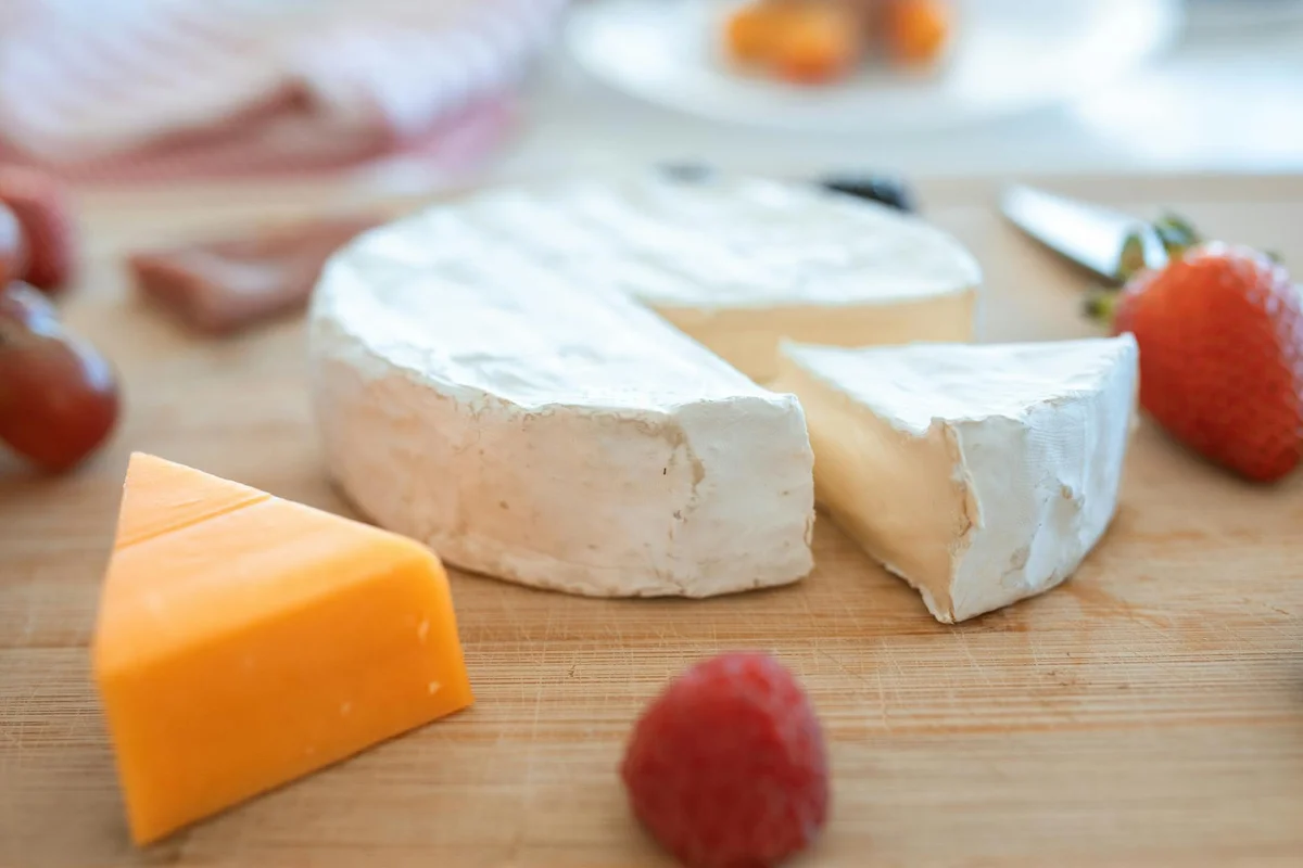 Wood cutting board with cheese and berries on a kitchen counter