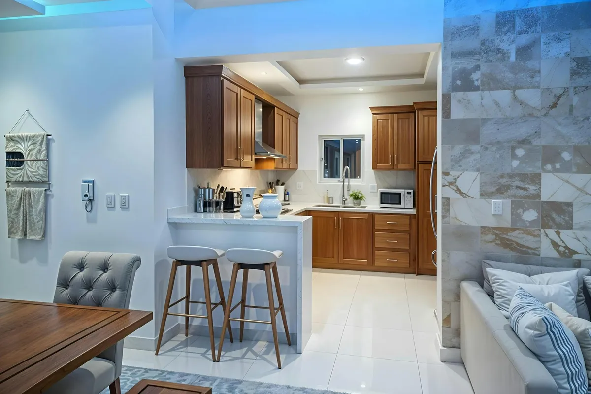 Interior view of a contemporary kitchen featuring wooden cabinets, a white island with two stools, and a cozy living area, illustrating wood furniture finishes.